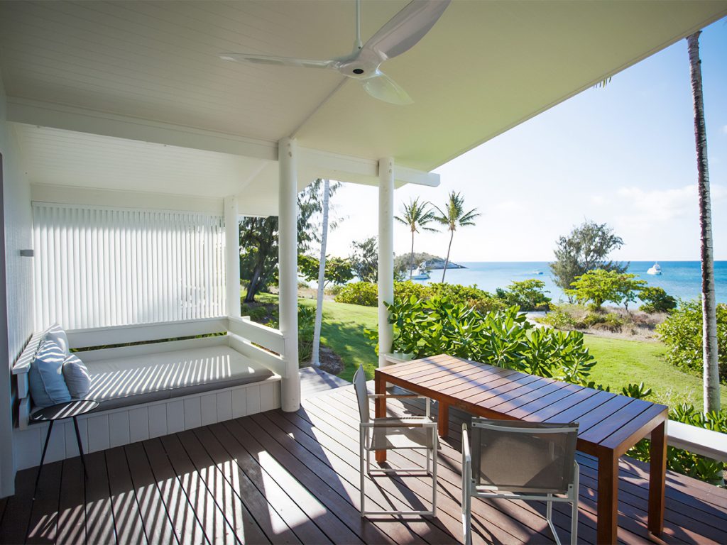 View from a beach front suite at Lizard Island. Daybed and seating on porch in the foreground and grass beach and ocean in the background.