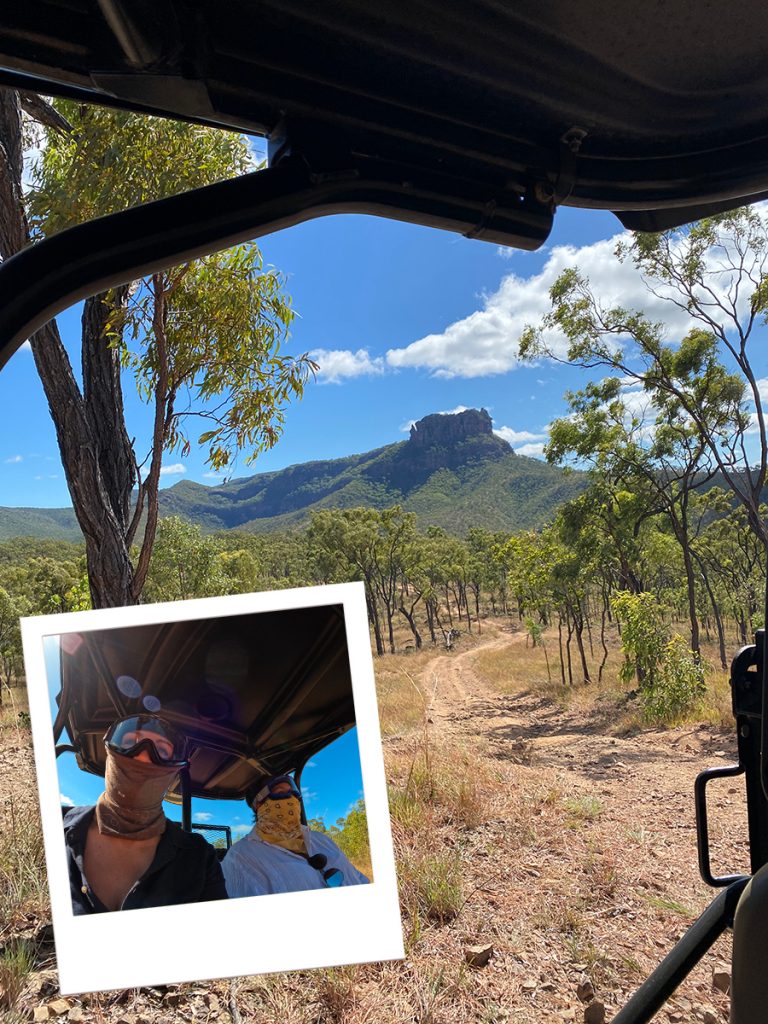 Queensland outback as viewed from an ATV, with trees in the foreground and mountain in the background. Inset image of Katie and colleague riding ATV through the outback. 